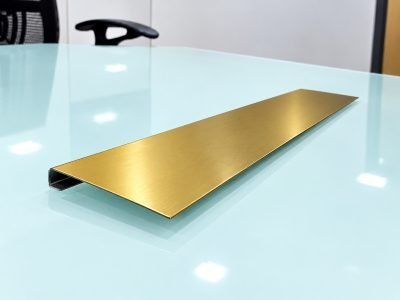 Gold hairline J profile with a returned edge on a glass table