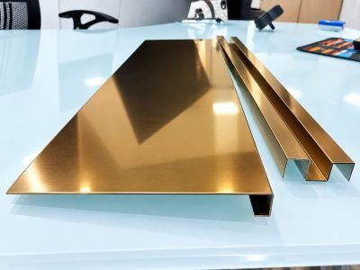 Gold mirror-finish J profile beside two gold channel profiles on a glass table