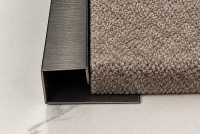 P channel edge trim in brushed stainless steel between carpet and tile — P Channel · Architectural Profiles
