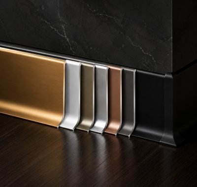 Skirting profiles in brass, bronze and grey finishes against a dark wall