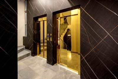 Lift entrances with gold mirror-finish door frames in a dark stone lobby