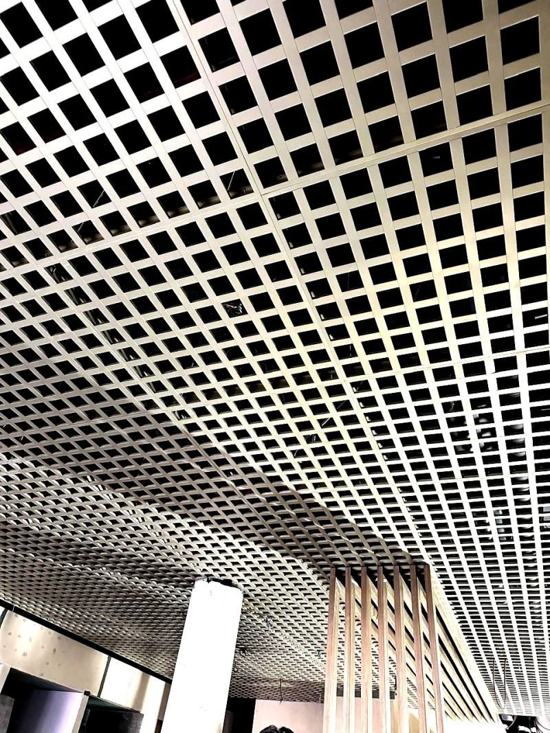 Open-cell metal grid ceiling over an open floor, seen from below