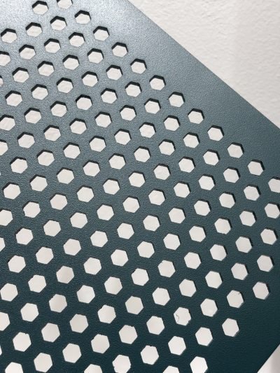 Dark green metal sheet with hexagonal perforations, angled view — Perforated Sheets · Perforated & Mesh