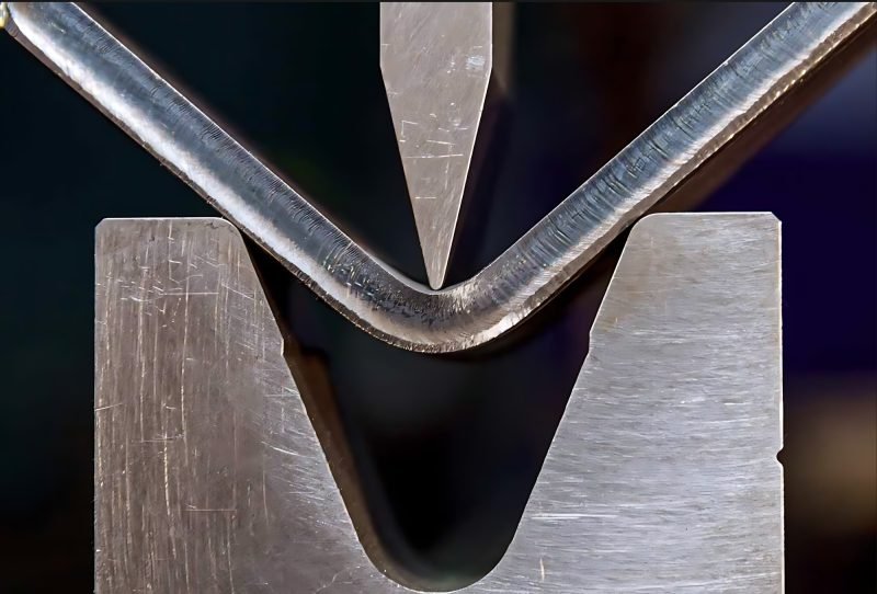The groove closing under the punch — the sheet folds into the channel, not around a radius